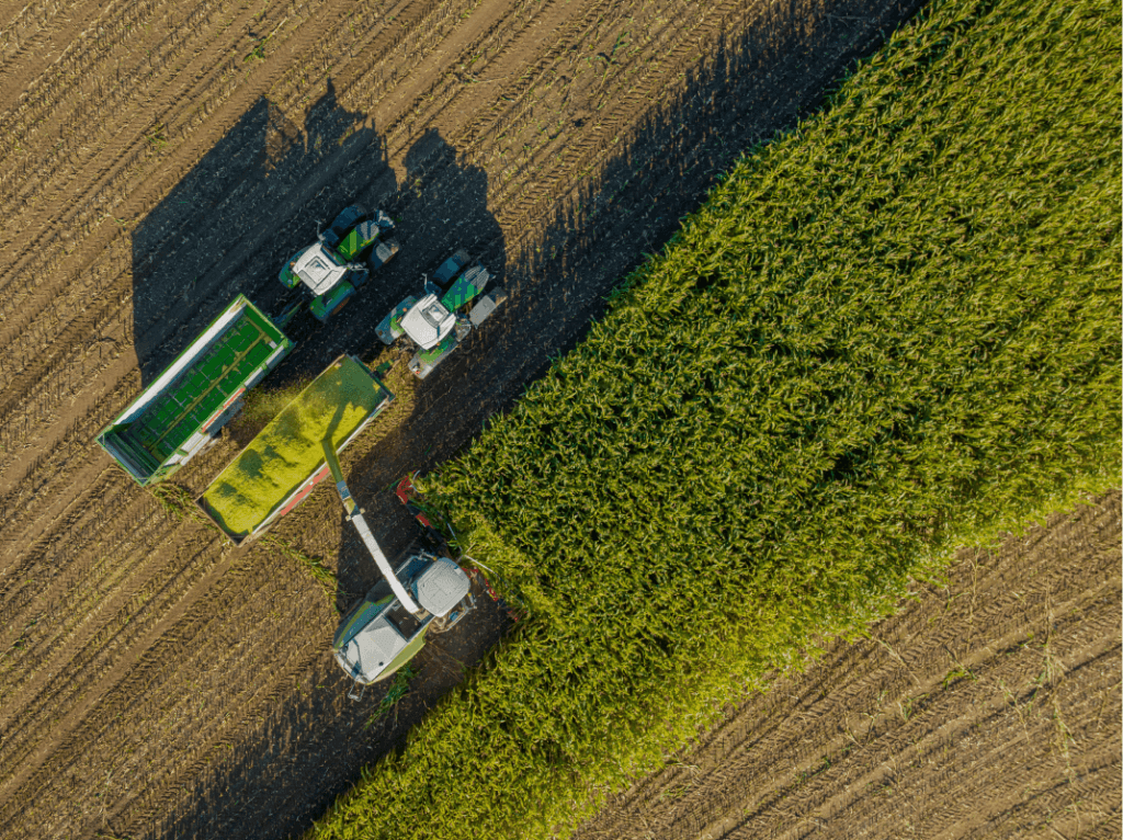 Aerial view of agricultural machinery, powered by alternative fuel, harvesting crops on a sunny day, illustrating the contrast between the golden harvested field and the lush green unharvested section.