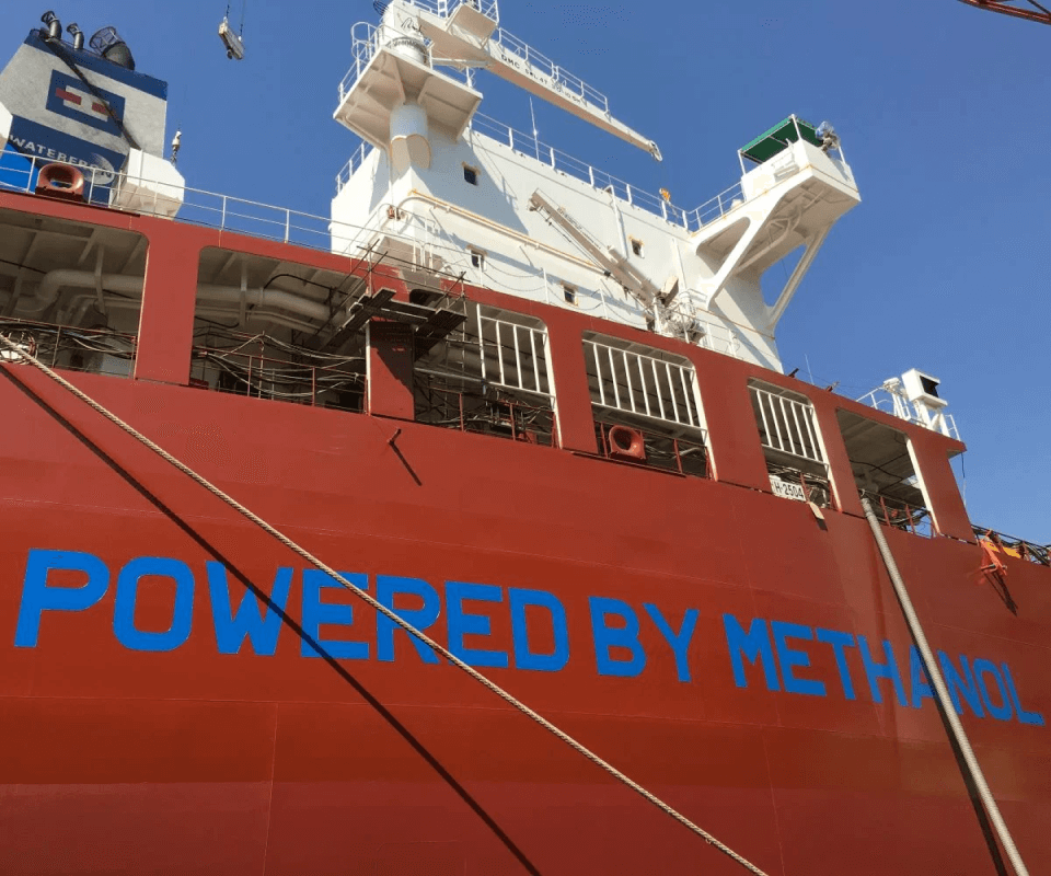 A large red ship with the text "powered by alternative fuel" emblazoned on its side, showcasing its use of an alternative fuel source for maritime transportation under a clear blue sky.