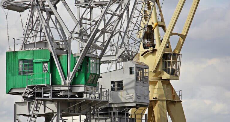 Two towering harbor cranes against a cloudy sky, showcasing industrial might and engineering prowess.
