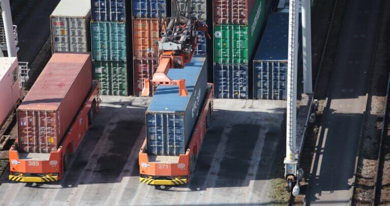 Aerial view of a bustling cargo terminal with colorful shipping containers and terminal tractors moving goods for international trade.