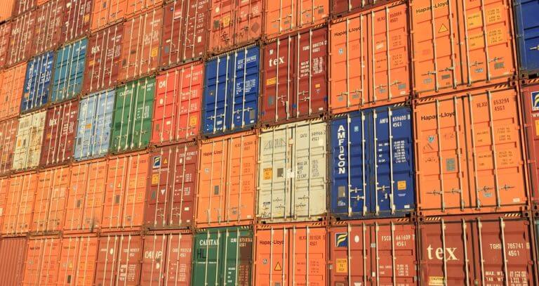 Stacked shipping containers in various colors create a geometric pattern against a clear sky.