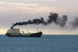Cargo ship at sea, emitting dark smoke from its funnel against a twilight sky.